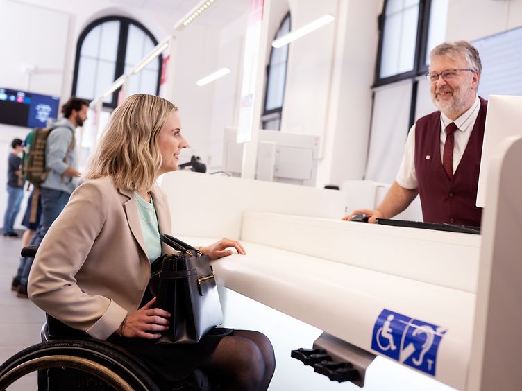 Frau mit Rollstuhl im Reisezentrum